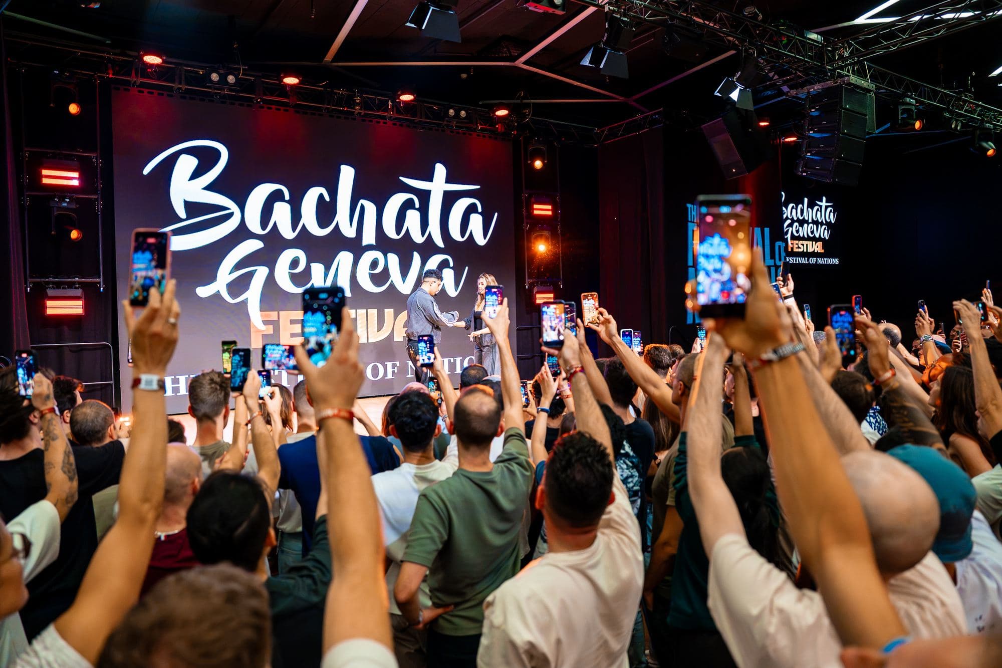 The crowd filming the artists on stage in front of the Bachata Geneva Festival screen